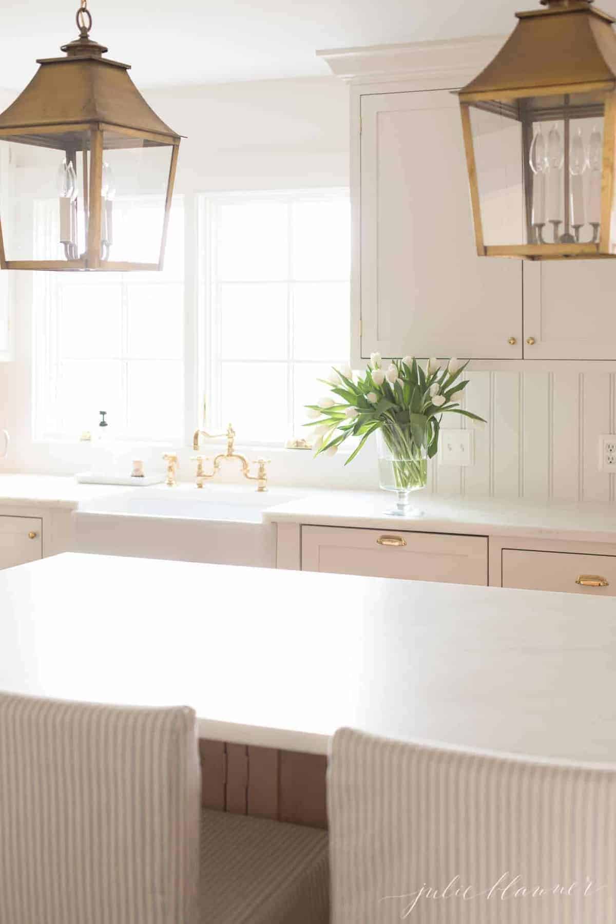 A white kitchen with white marble countertops, flowers by the sink