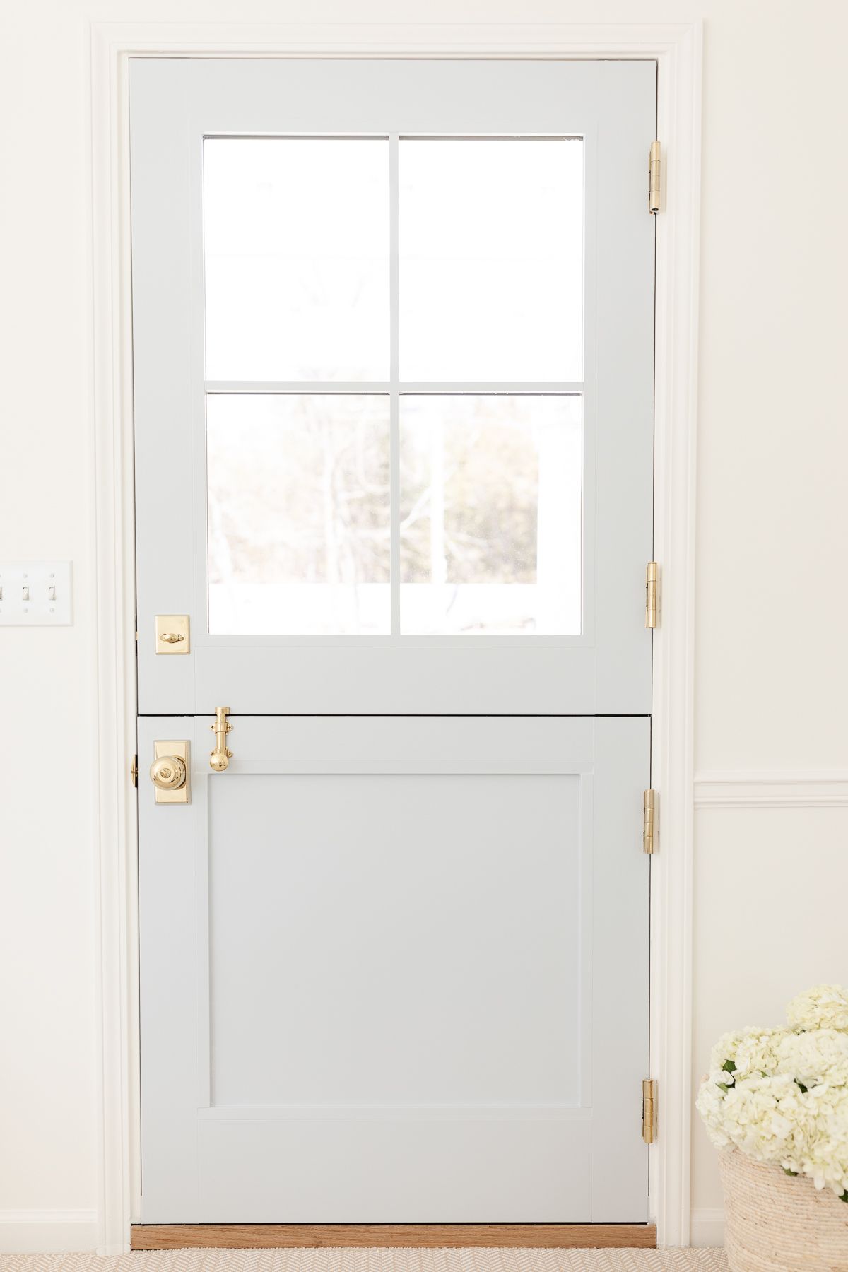 A blue Dutch door with four glass panes on top, looking from the inside out, with brass Dutch door hardware