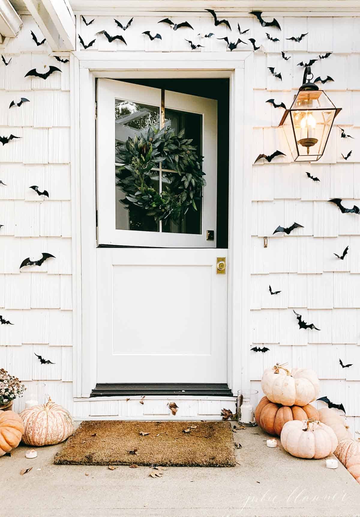 A white dutch door on a white cottage home, pumpkins and paper bats surrounding for halloween decor.