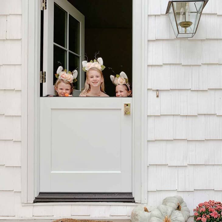 A white cottage with a white dutch door, three little girls peeking over the top.