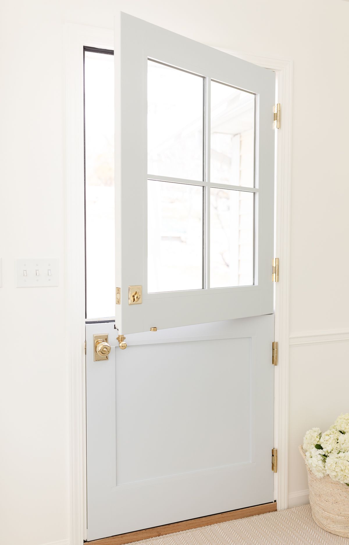 A blue Dutch door with four glass panes on top, looking from the inside out, with brass Dutch door hardware