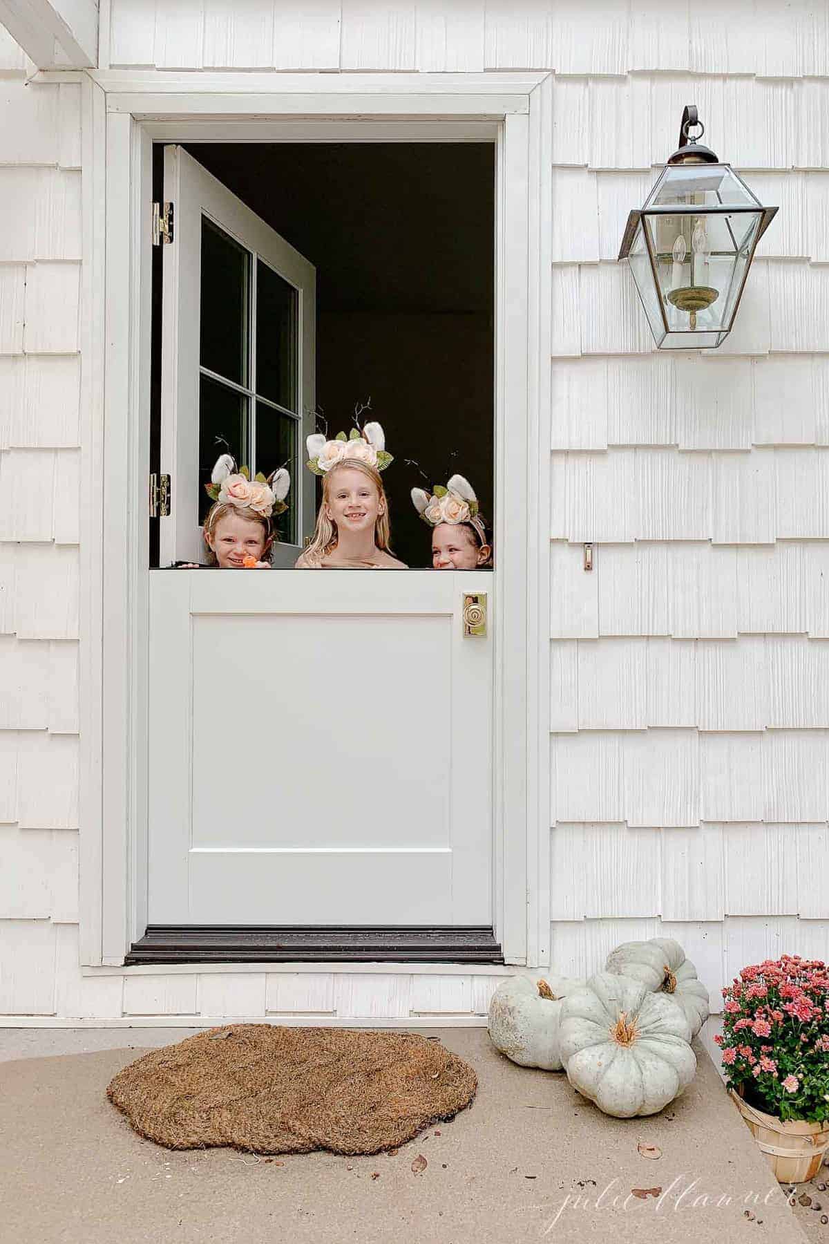 A white cottage with a white dutch door, three little girls peeking over the top.