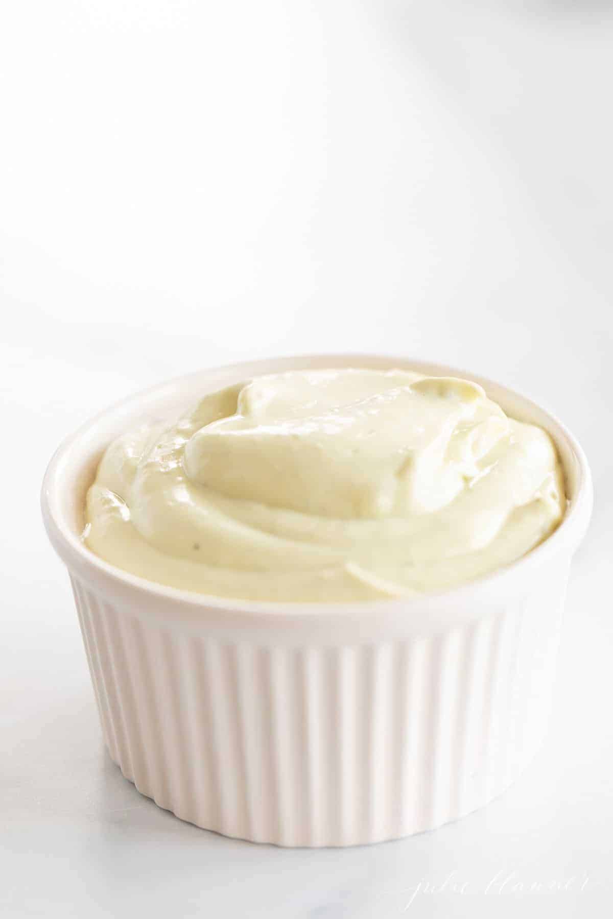 A white ramekin filled with avocado mayo on a marble surface.