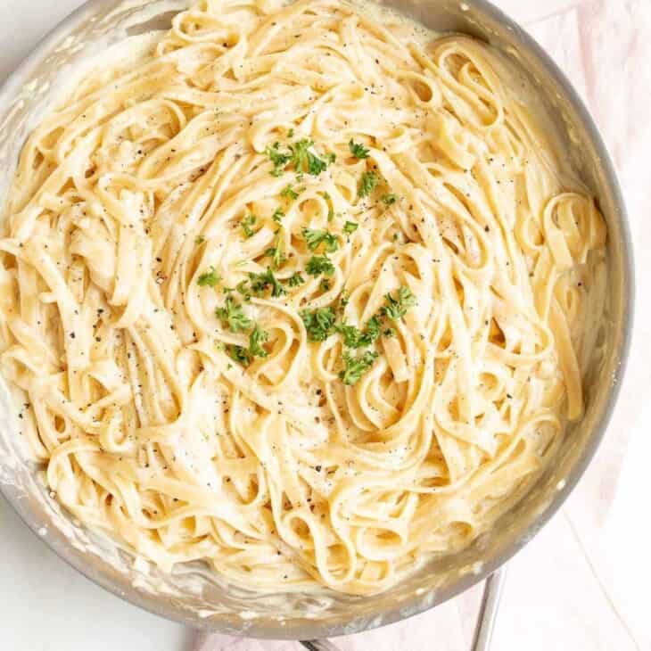 pasta in cream sauce in sauté pan garnished with parmesan and parsley