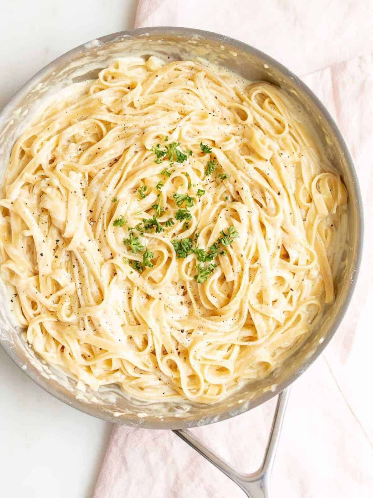 pasta in cream sauce in sauté pan garnished with parmesan and parsley