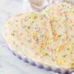 sugar cookie cake topped with frosting and sprinkles in purple heart shaped dish