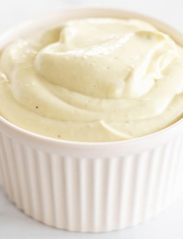 A white ramekin filled with avocado mayo on a marble surface.