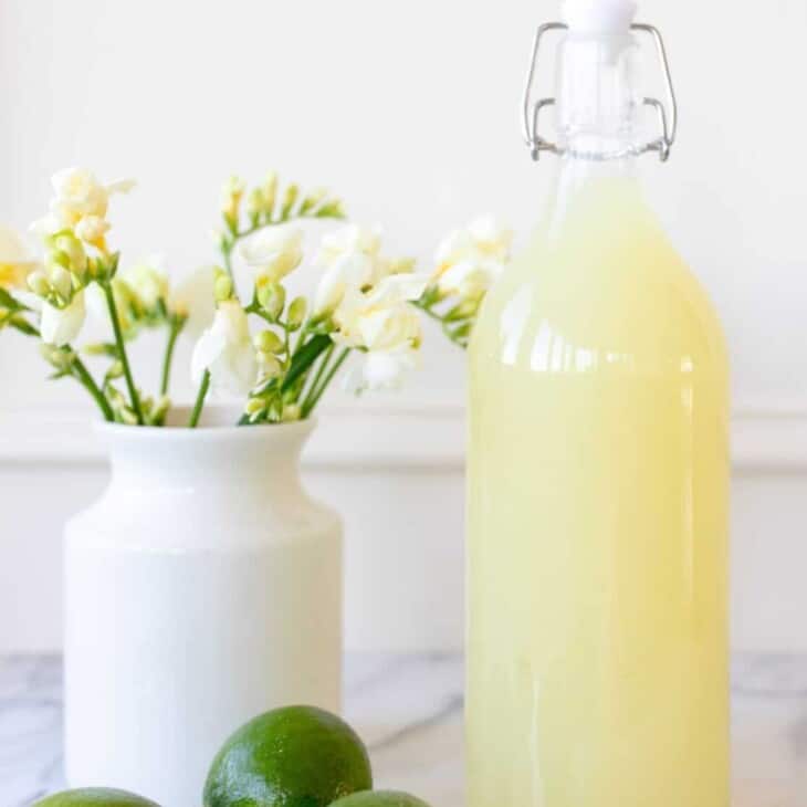 margarita mix in a bottle next to limes and flowers