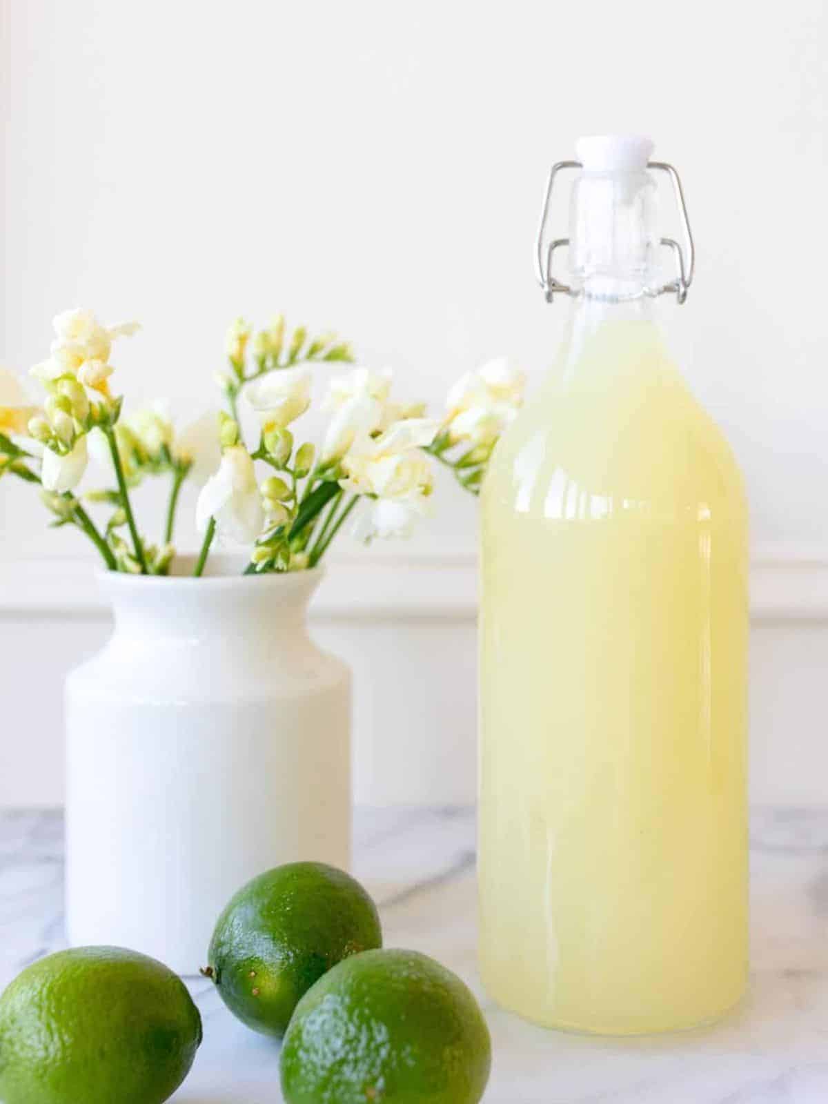 margarita mix in a bottle next to limes and flowers