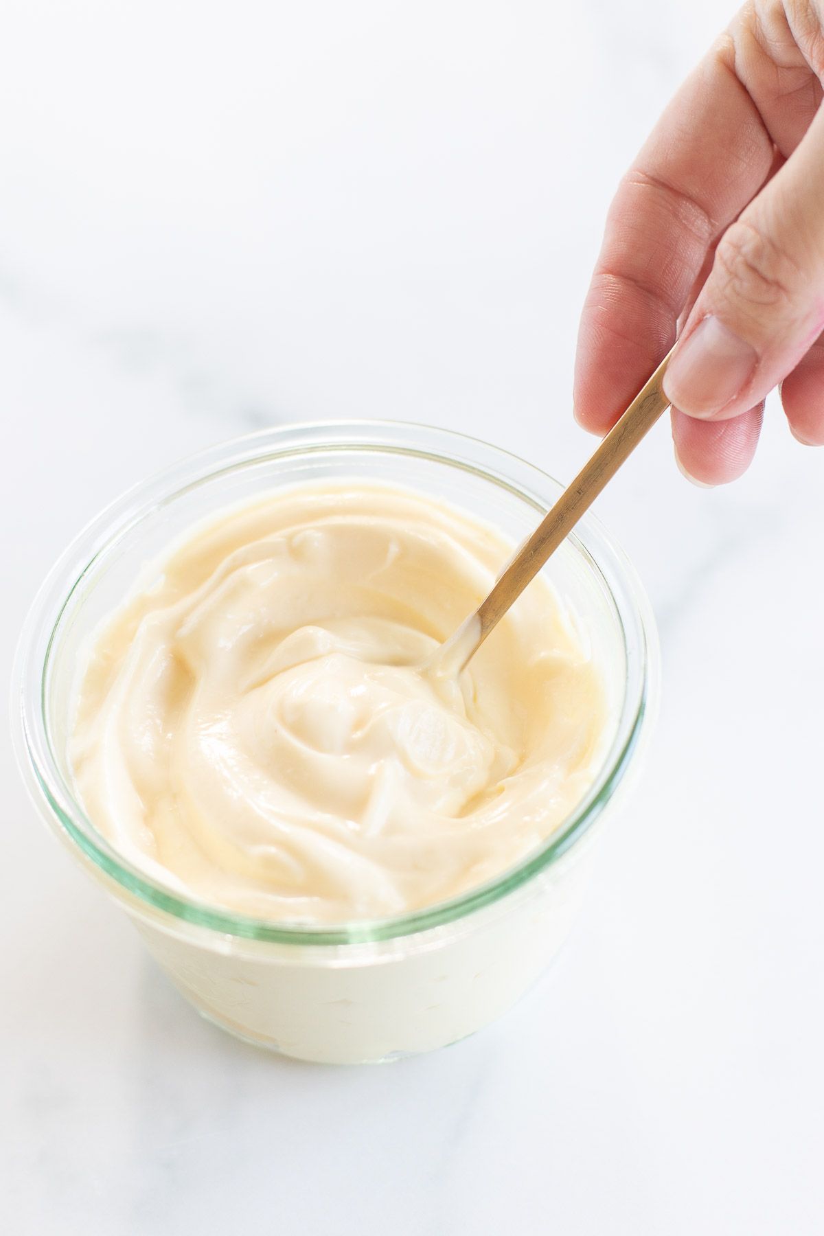 A hand stirring homemade mayonnaise in a tutorial for how to make mayonnaise.