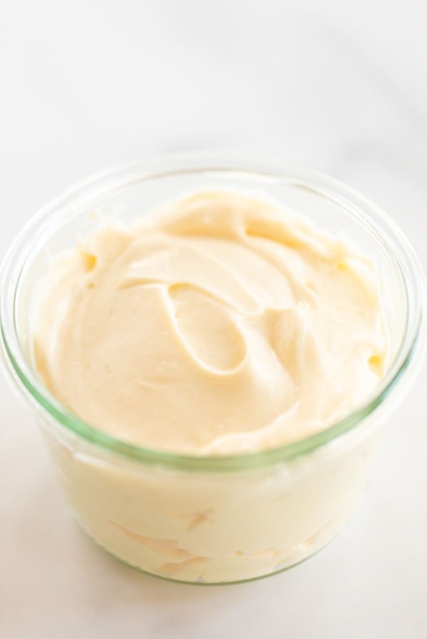 A small glass jar of mayonnaise for a tutorial on how to make mayo, it's resting on a marble countertop.