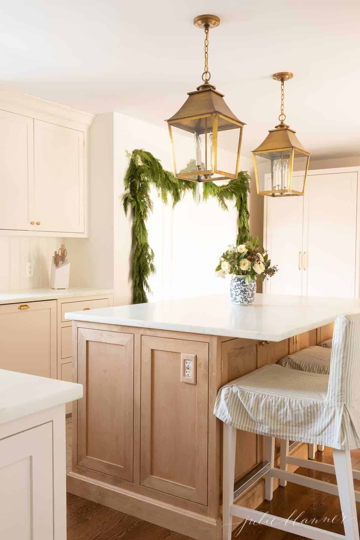 A soft wood island in a cream kitchen decorated with Christmas greenery.