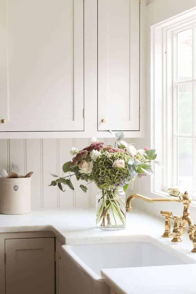 Cream inset cabinets in a kitchen with marble counters and a brass faucet.