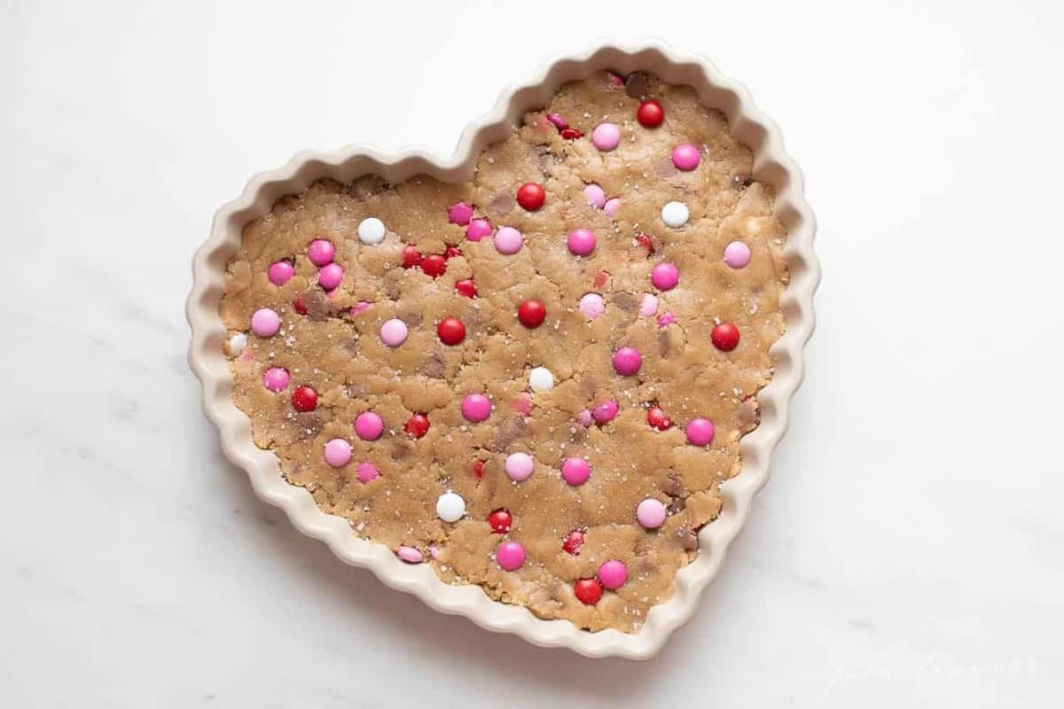 Thick and Chewy M&M Cake in a heart shaped dish, topped with Valentine's Day M&Ms.