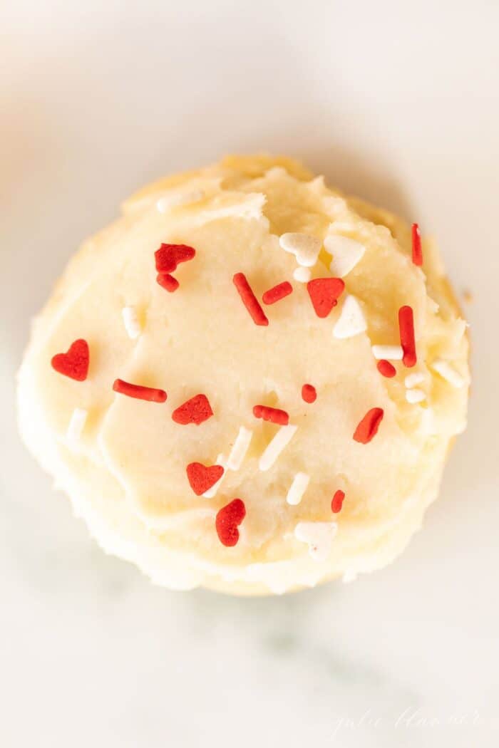 A single melt in your mouth sugar cookie frosted with sprinkles on a marble surface.