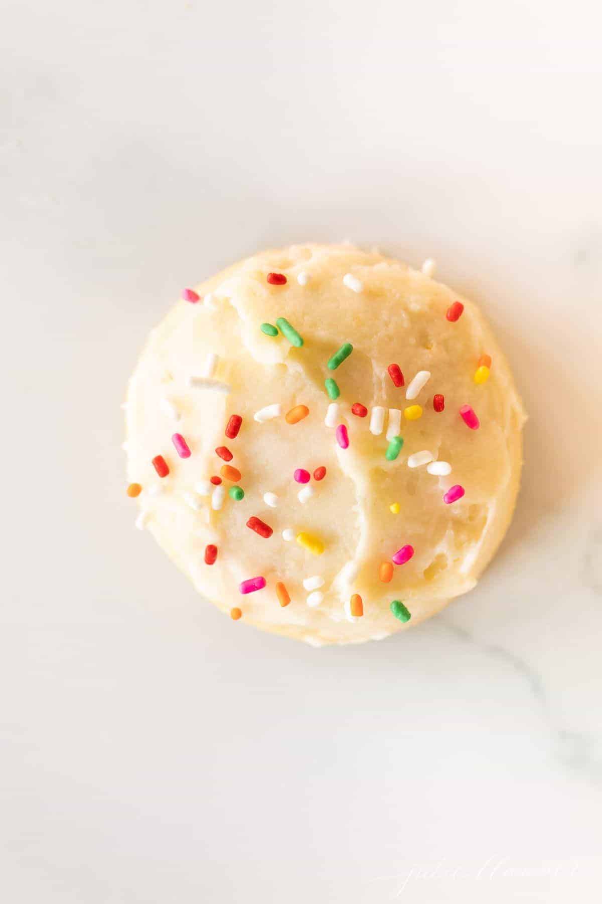 A single Amish sugar cookie frosted with sprinkles on a marble surface.