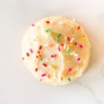 A single melt in your mouth sugar cookie frosted with sprinkles on a marble surface.