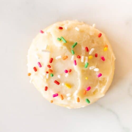 A single melt in your mouth sugar cookie frosted with sprinkles on a marble surface.