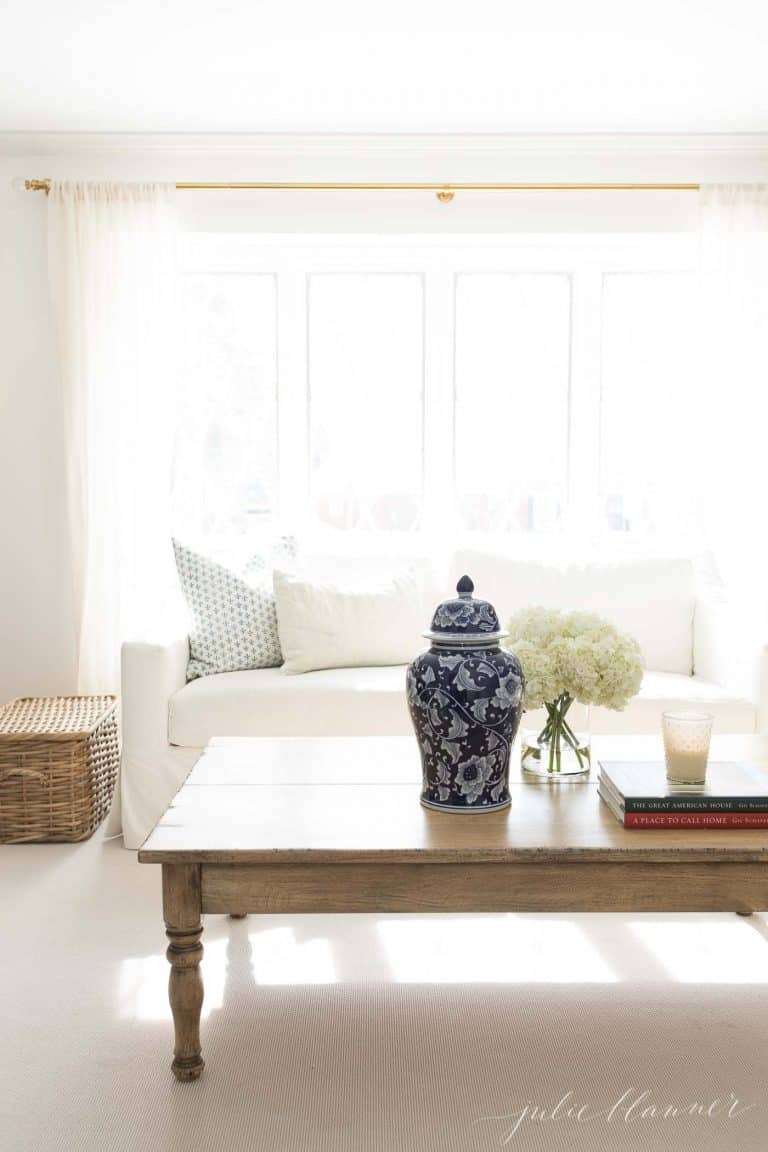 A neutral living room with a white sofa, wood coffee table and a pop of blue.