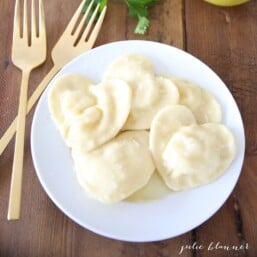 A white plate of homemade ravioli, shaped into hearts for Valentine's Day, with gold forks to the side.