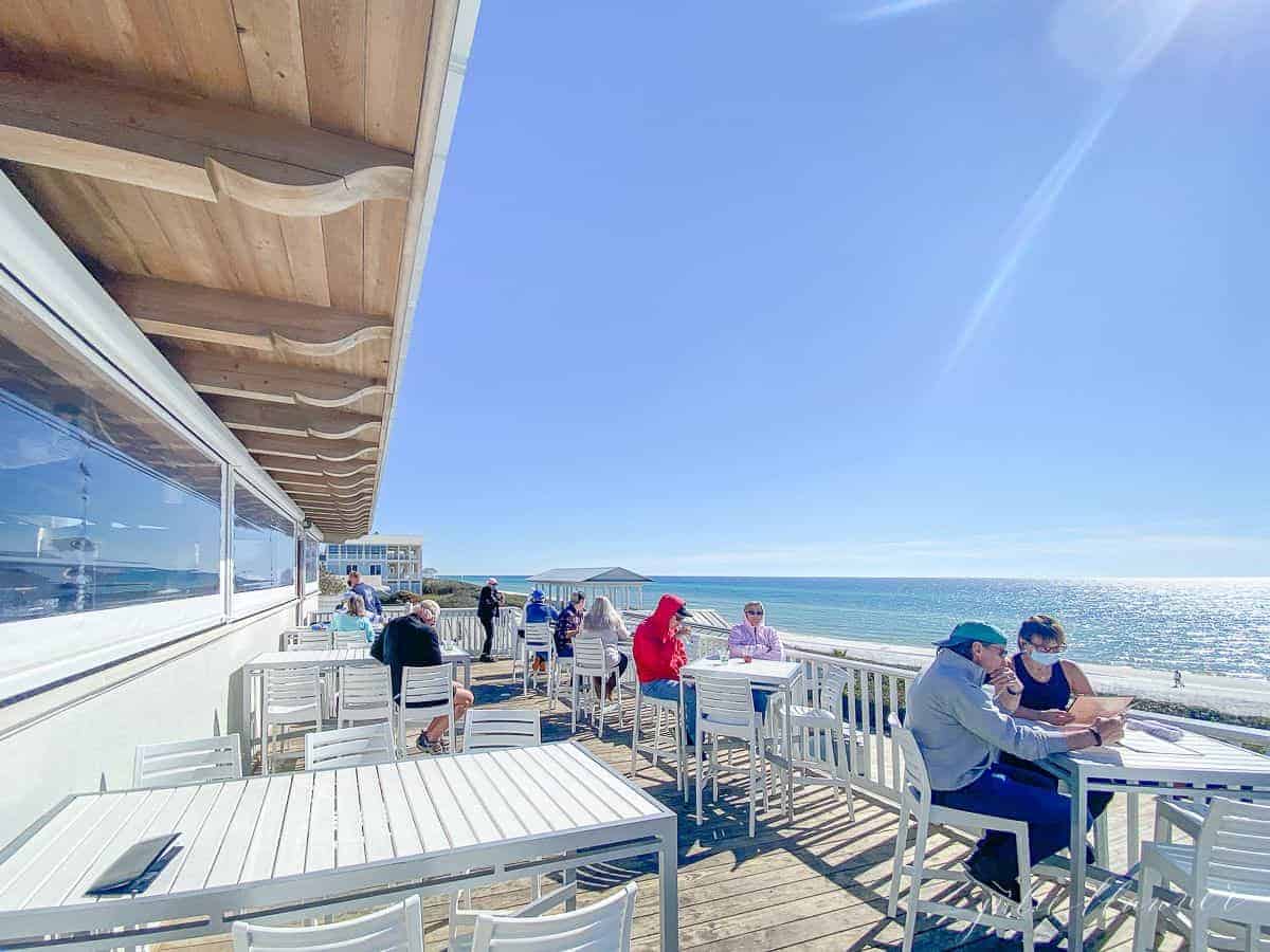 A pretty restaurant patio on the beach in Seaside Florida, diners at small tables along patio.