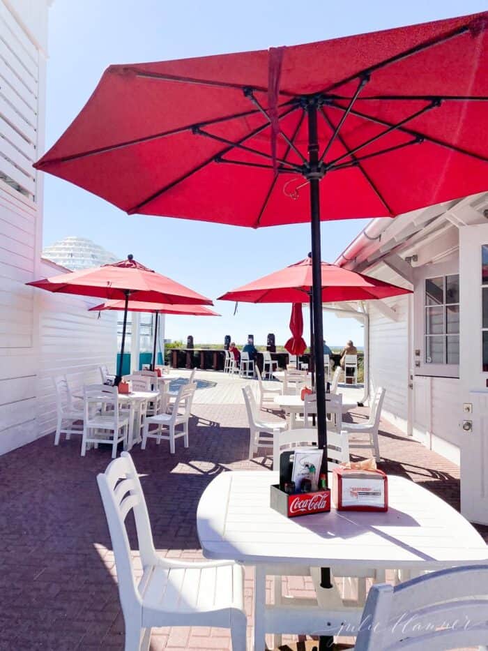 Red umbrellas on white patio tables and chairs on a restaurant patio in Seaside Florida.