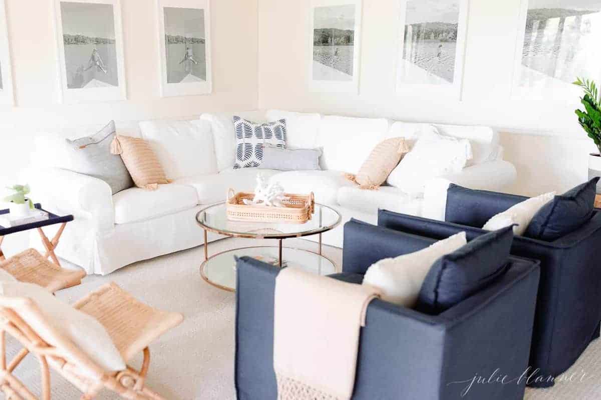 A modern white living room with large black and white photos on the wall, a white sectional sofa and navy blue chairs.