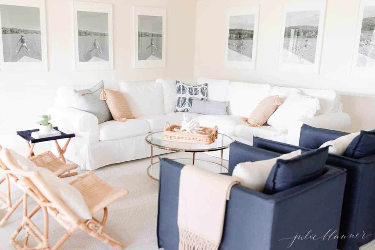 A modern white living room with large black and white photos on the wall, a white sectional sofa and navy blue chairs.