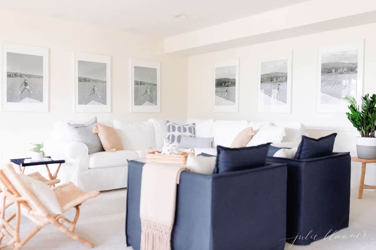 A modern white living room with large black and white photos on the wall, a white sectional sofa and navy blue chairs.