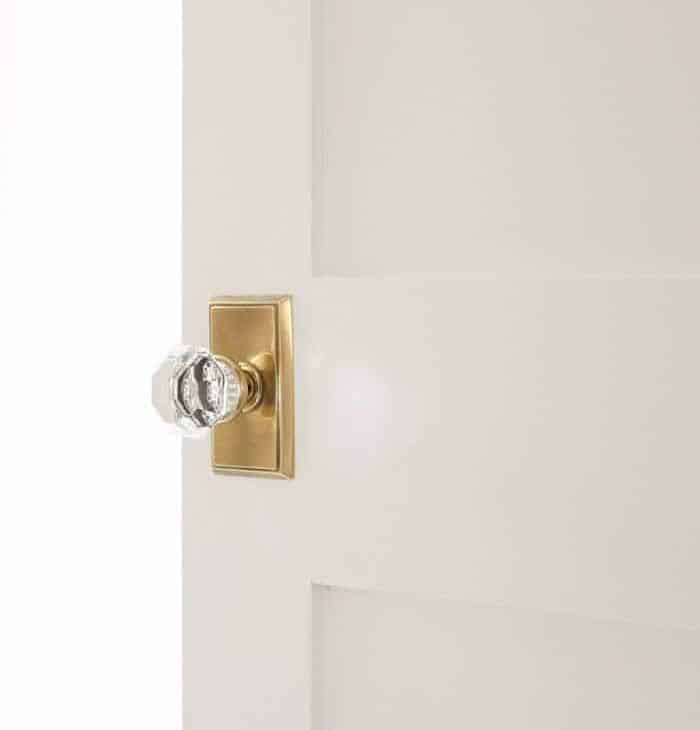 A white Shaker door with a brass doorknob, opening into a bedroom.