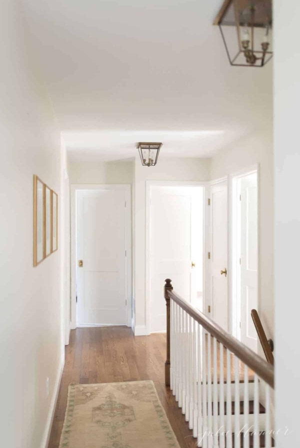 A white hallway with wood floors and Shaker style doors with brass door knobs.