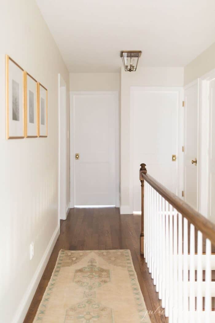 A white hallway with wood floors and Shaker style doors with brass door knobs.