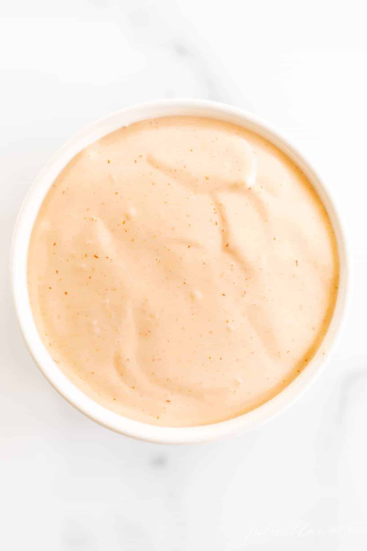 A white bowl full of homemamde sriracha mayo on a white background.