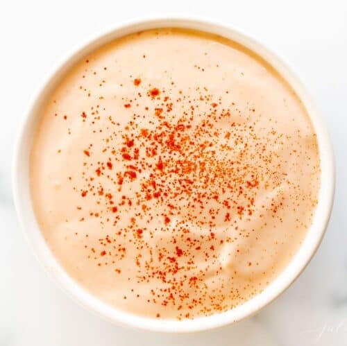 A white bowl full of homemade sriracha mayo on a white background.