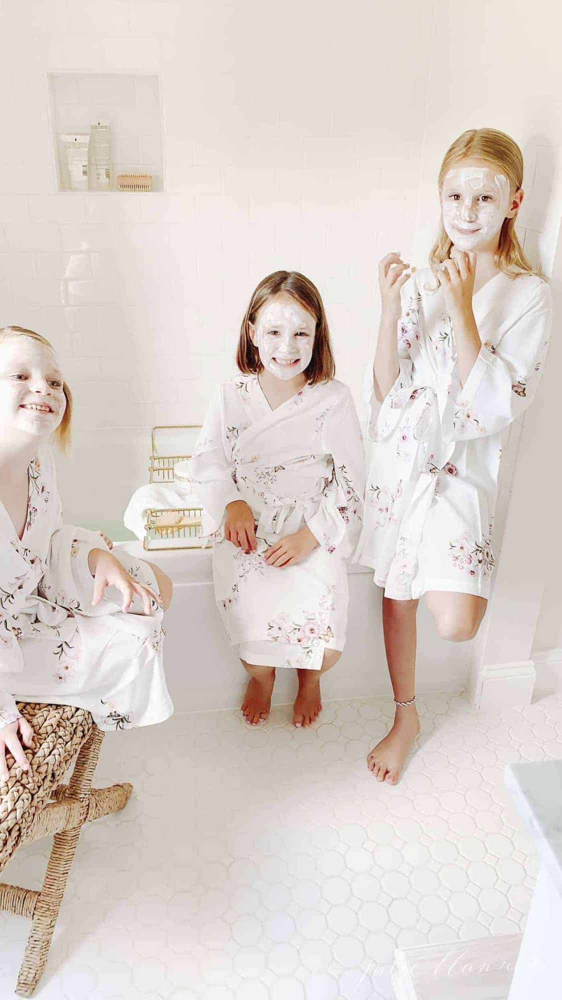Three little girls in floral robes in a bathroom with face masks for a spa day.