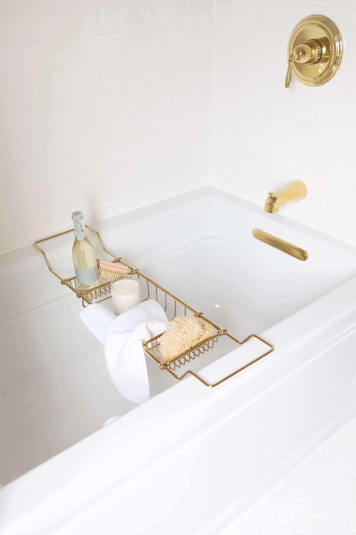 A white bathtub surrounded by white subway tile with brass fittings.