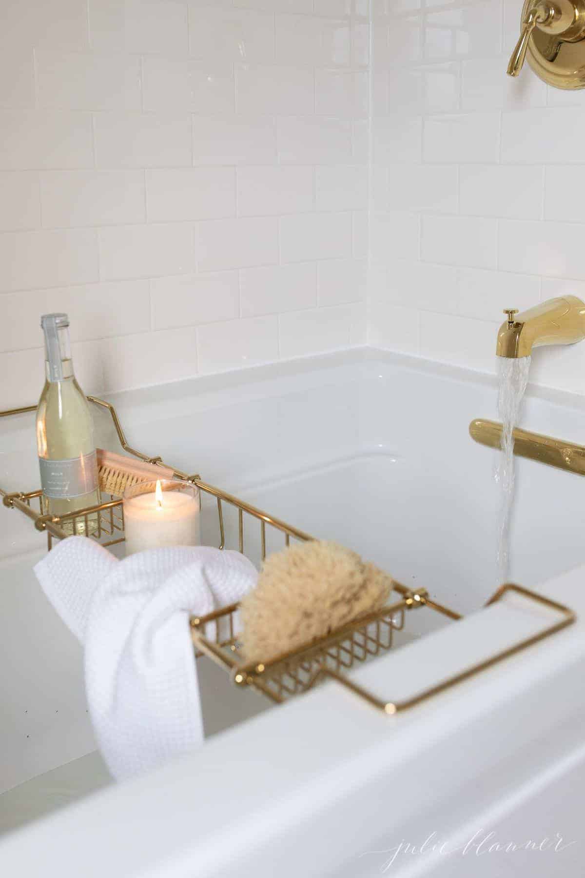 A white bathtub surrounded by white subway tile with brass fittings.