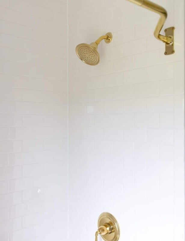 A white subway tile shower with brass hardware.
