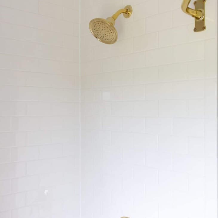 A white subway tile shower with brass hardware.
