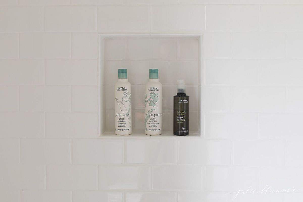 A shower niche with shampoo bottles in a shower with white subway tile.