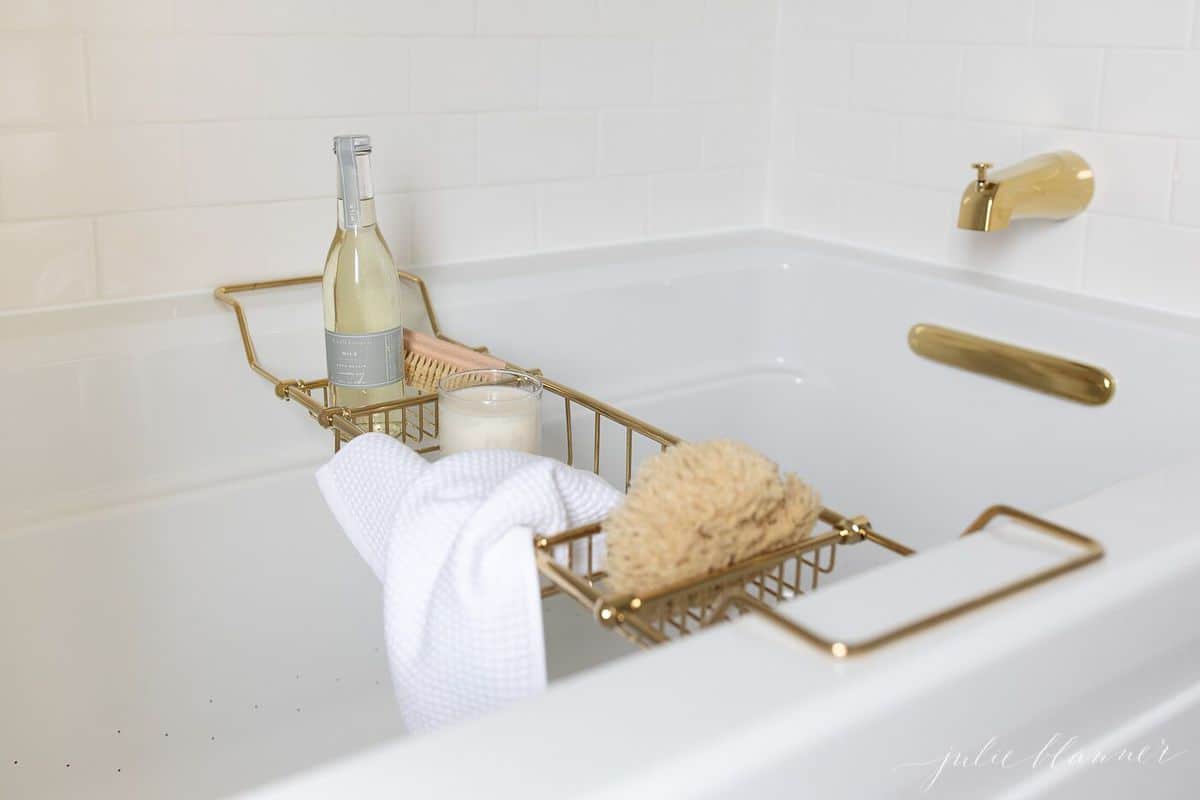 A white bathtub surrounded by white subway tile with brass fittings.