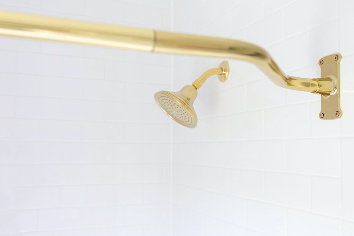 Golden showerhead with matching arm and wall mount on a white subway-tiled bathroom wall.