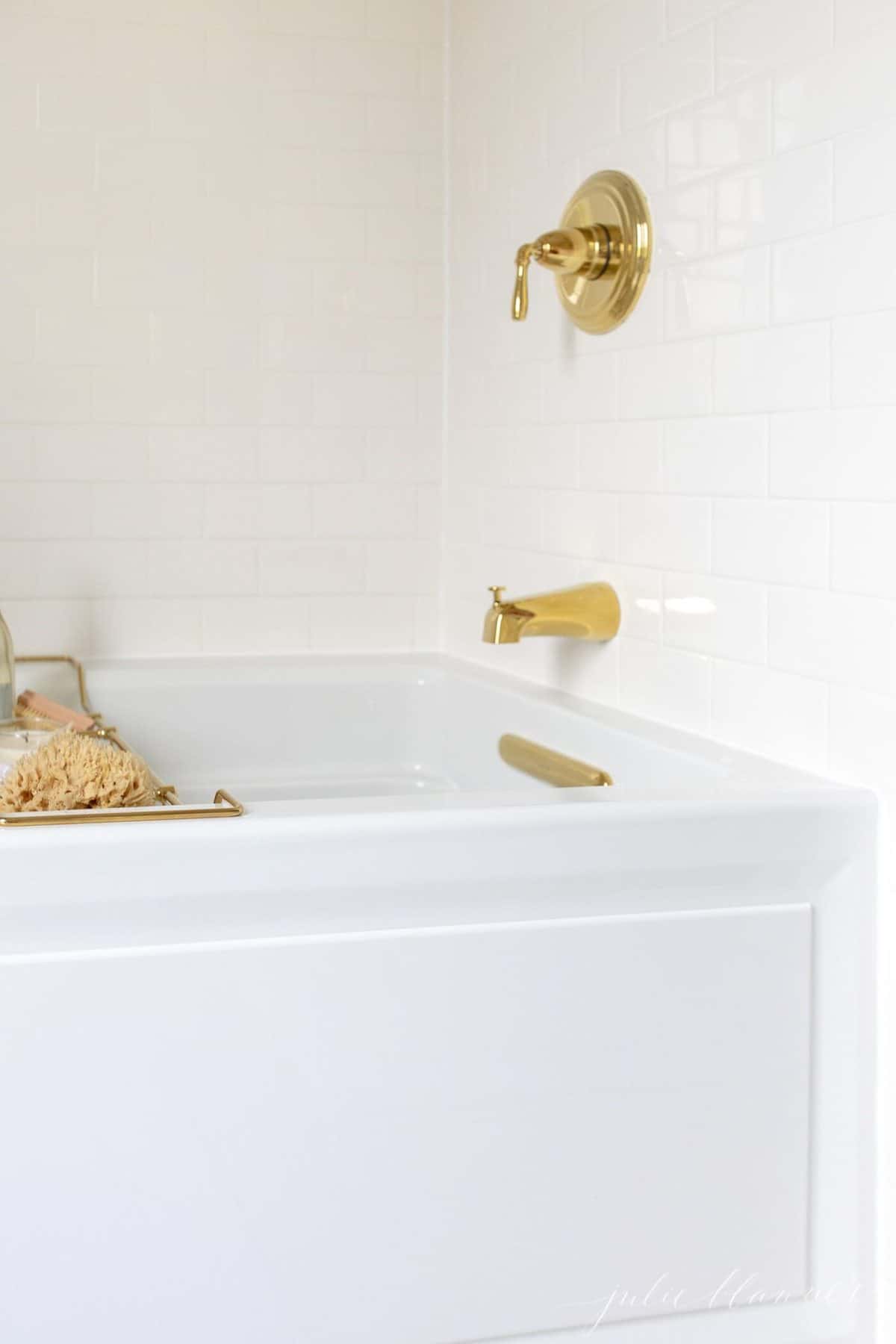 A white bathtub surrounded by white subway tile with brass fittings.