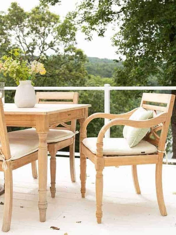 Teak wood furniture dining set on a white patio with a glass railing.