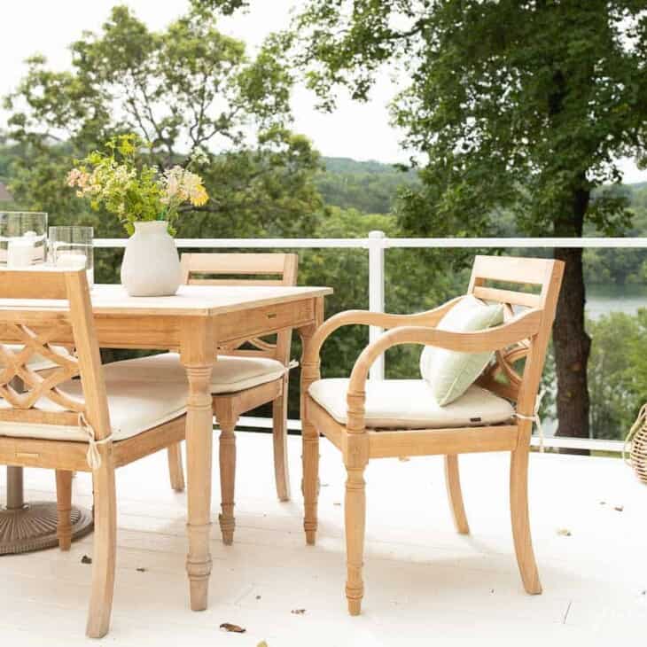 Teak wood furniture dining set on a white patio with a glass railing.