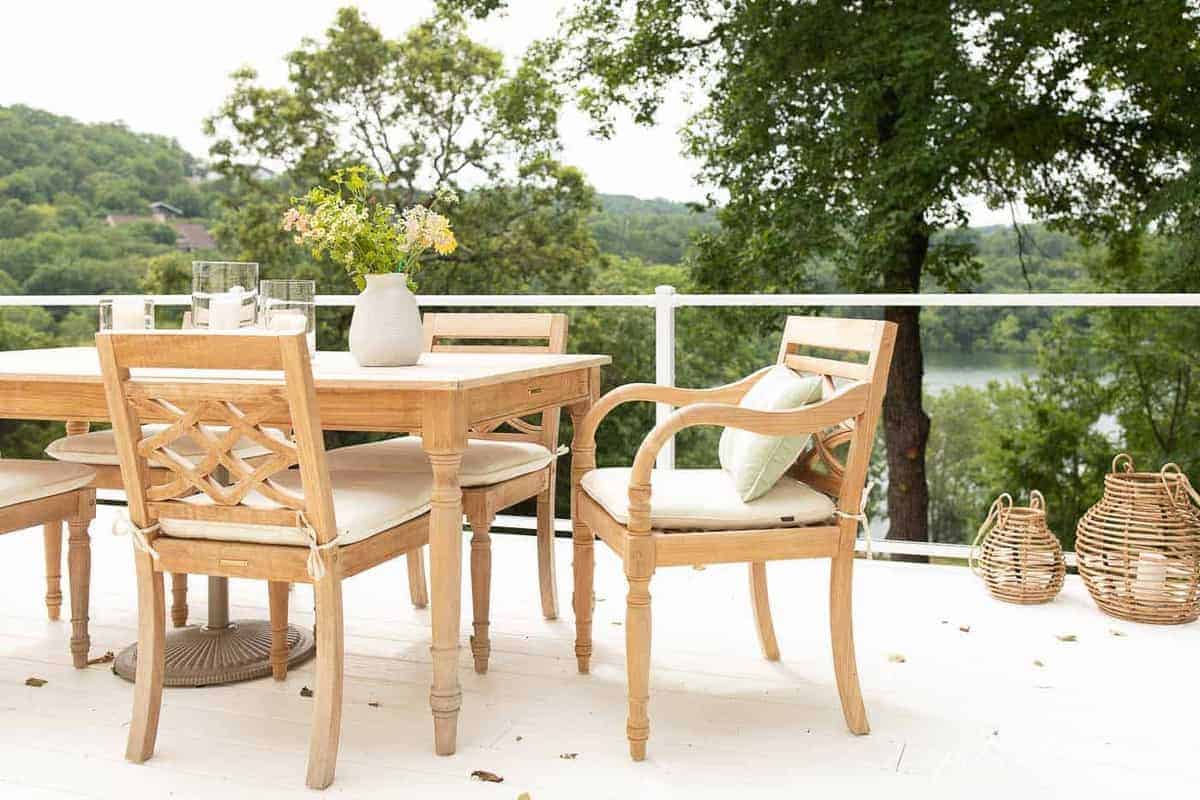 Teak wood furniture dining set on a white patio with a glass railing.