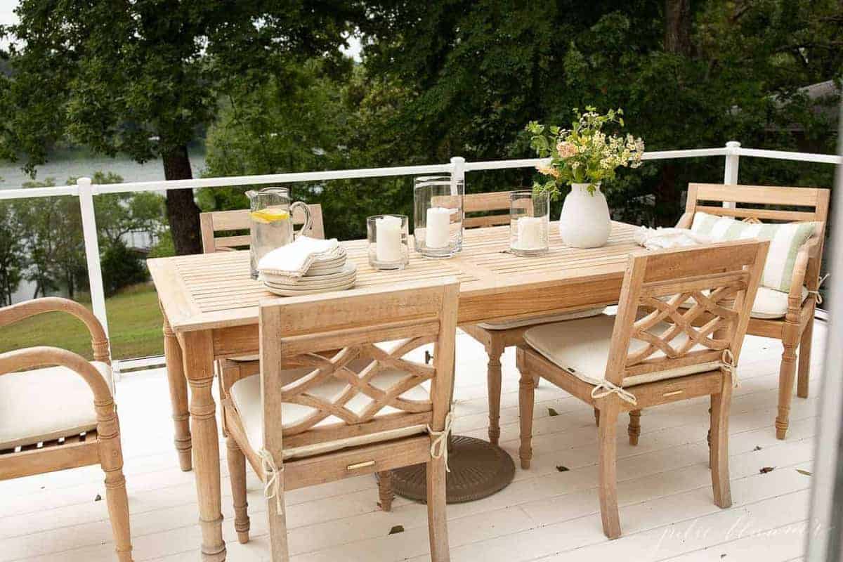 Teak outdoor furniture dining set on a white patio with a glass railing.