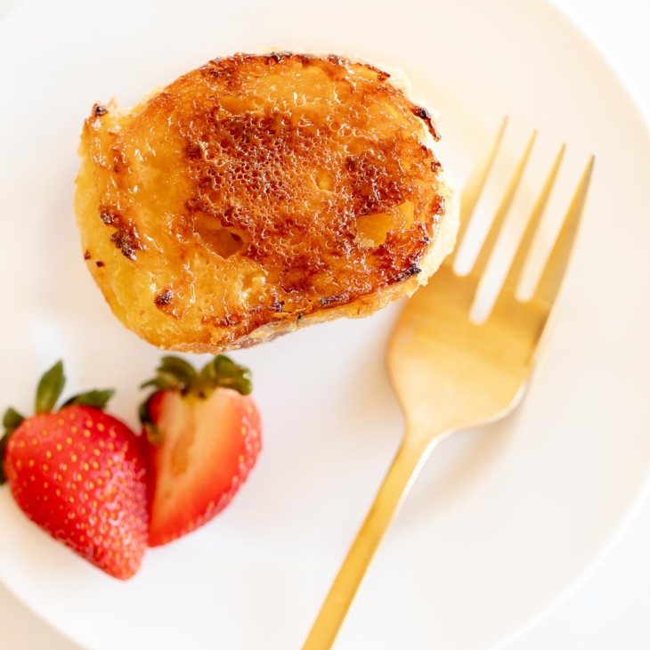 A slice of creme brulee french toast on a white plate with a gold fork.