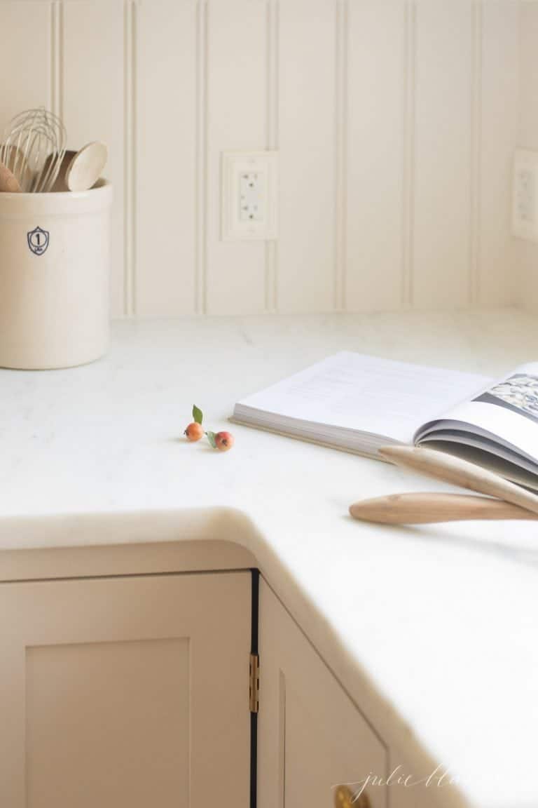 A beadboard backsplash and white marble countertops, with a cookbook open on the counter.