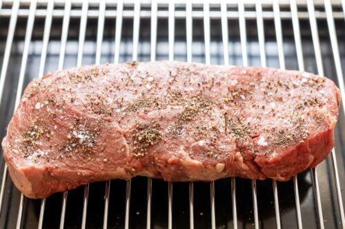 A large steak on a broiling rack, topped with seasoning for a broiled steak tutorial.